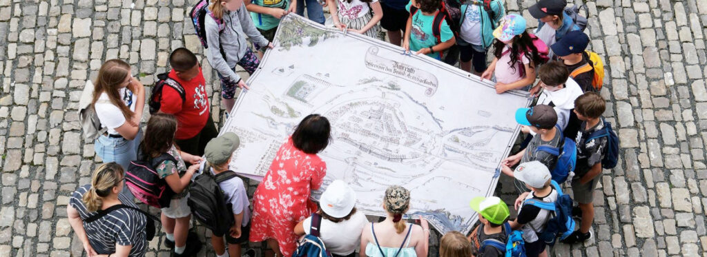 Große Gruppe von Kindern blicken auf den Stadtplan der Stadt Bayreuth vor dem Brand 1621