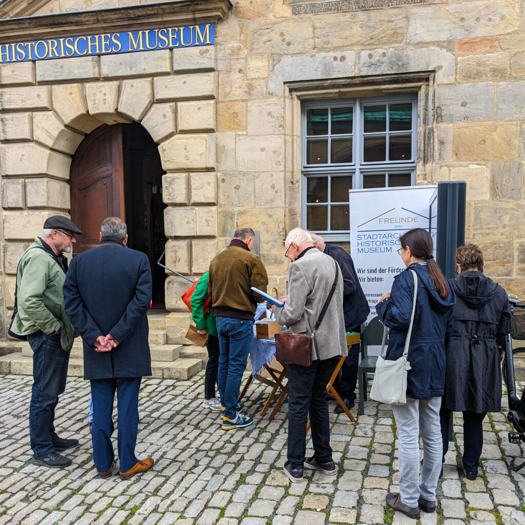 Besucher stehen vor dem Museum und schauen sich den Bücherstand des Fördervereins an.